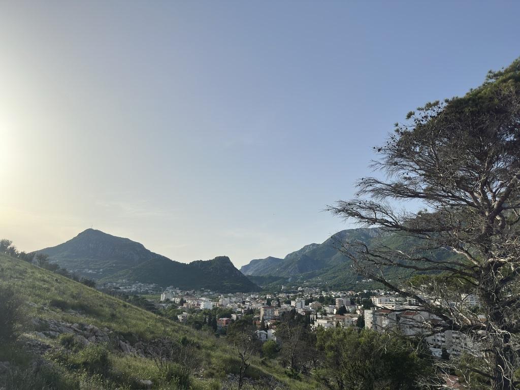 Blick von einem Hang auf eine Küstenstadt zwischen Bergen am Abend.