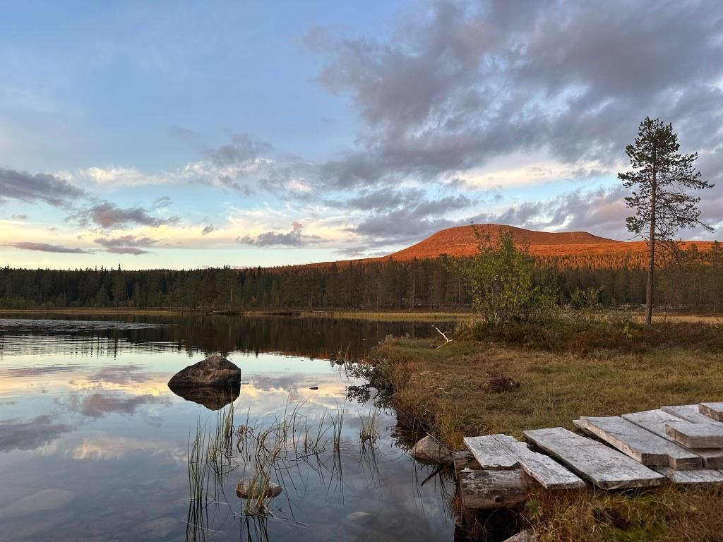 Stiller See mit rot angeleuchtetem Fjell im Abendlicht, Bohlensteg im Vordergrund.